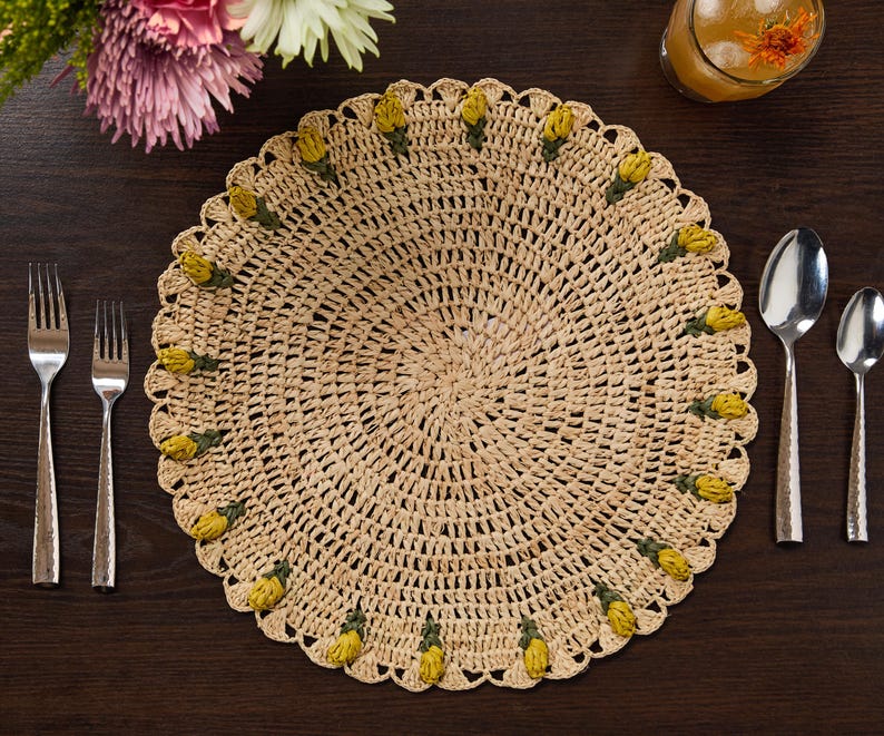 Handmade raffia crochet placemat with yellow tulip accents, set on a dark wooden table with utensils.