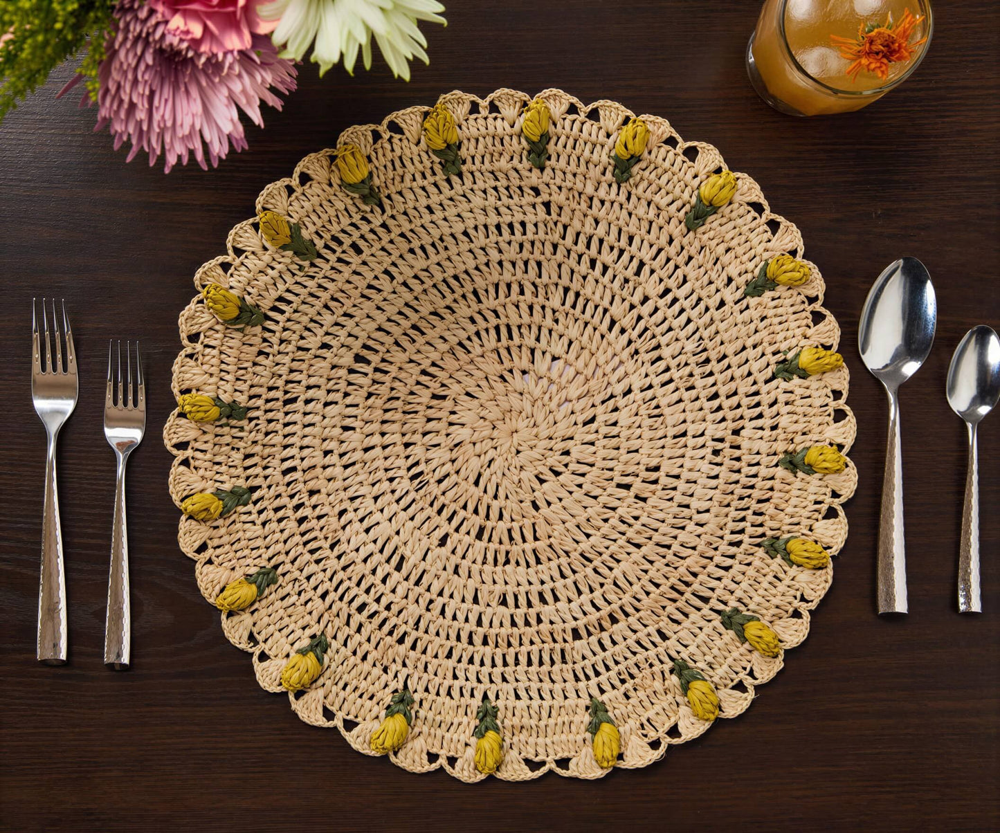 Handmade raffia crochet placemat with yellow tulip accents, set on a dark wooden table with utensils.