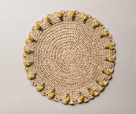 Handmade raffia crochet placemat featuring yellow tulip accents on a round, natural fiber design.