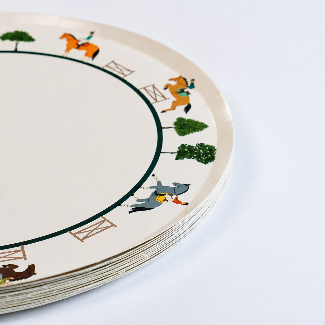 Stack of round cream paper plates with a border of illustrated horses, riders, jumps, and trees.