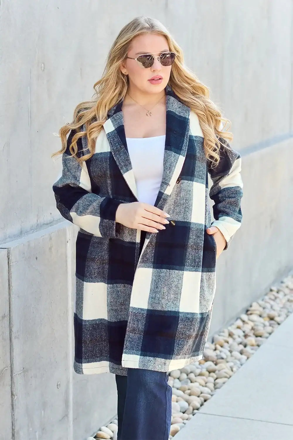 Woman wearing a plaid coat standing against a concrete wall.