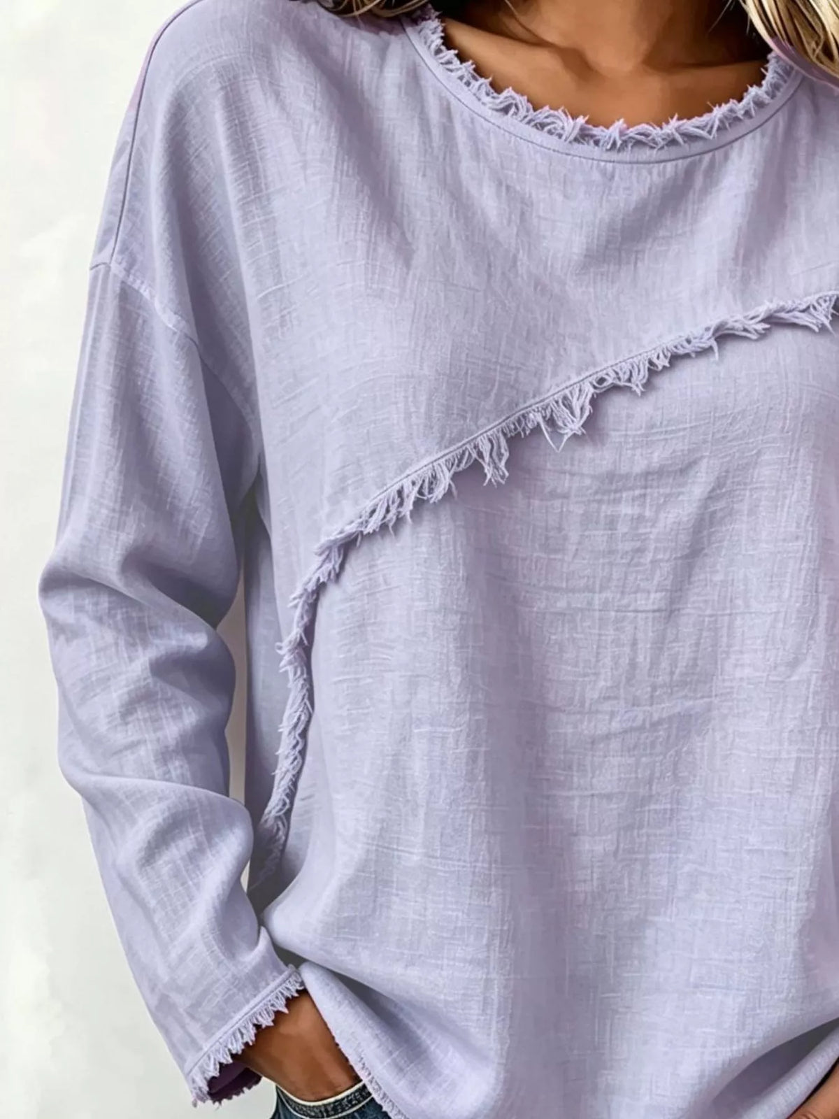 A close-up of a person wearing a light lavender long-sleeve top with raw, frayed edges and a diagonal frayed detail across the chest.