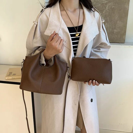 Person holding two brown leather bags with a neutral background