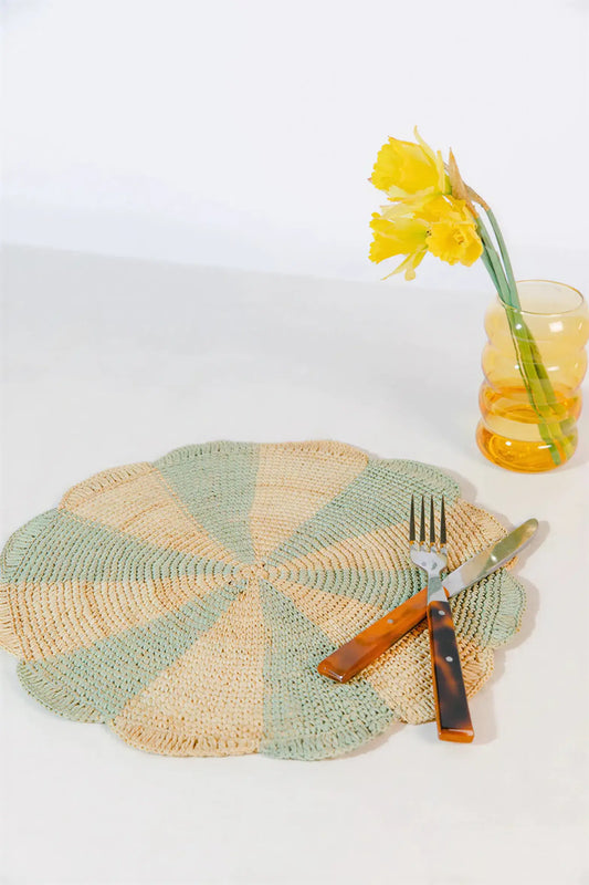 Pinwheel blue placemat made of raffia, featuring alternating light blue and beige sections, with utensils and a flower vase.