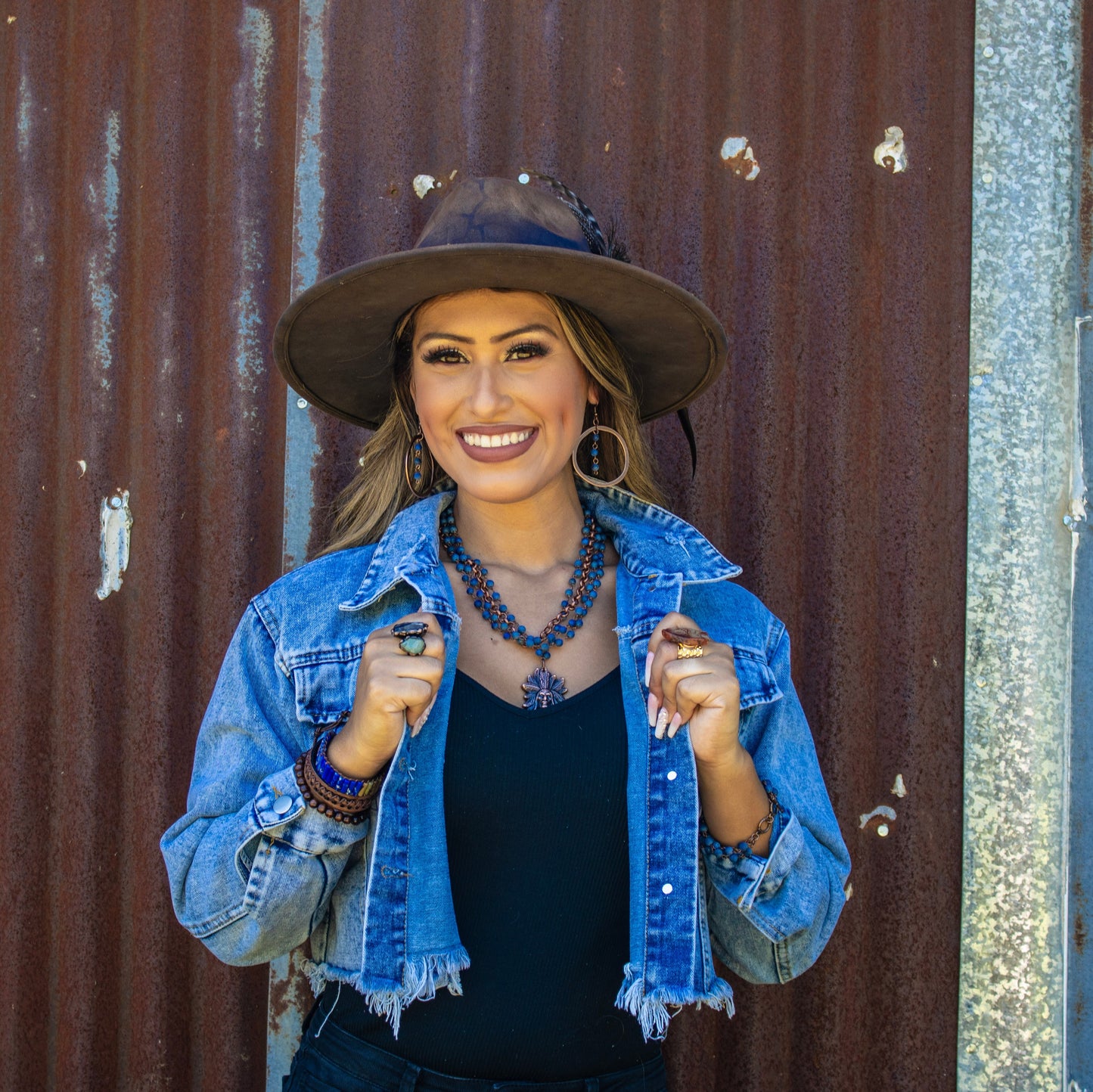 Woman wearing a denim jacket and hat against a rusty metal wall