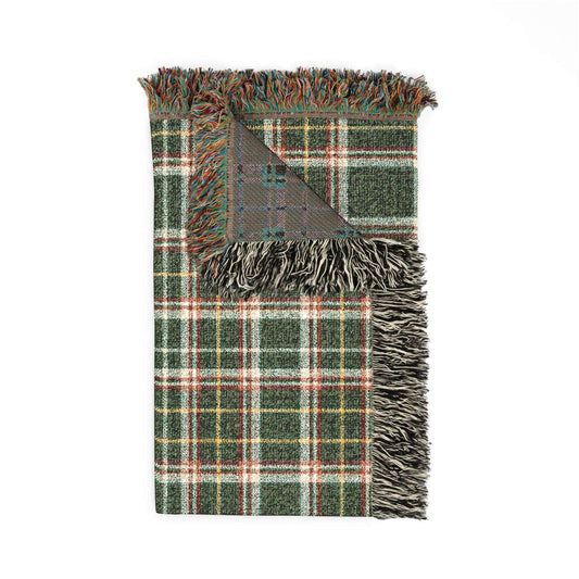 A folded plaid throw blanket with fringed edges, featuring a green, white, and red tartan pattern with a gray reverse side, shown on a plain white background.