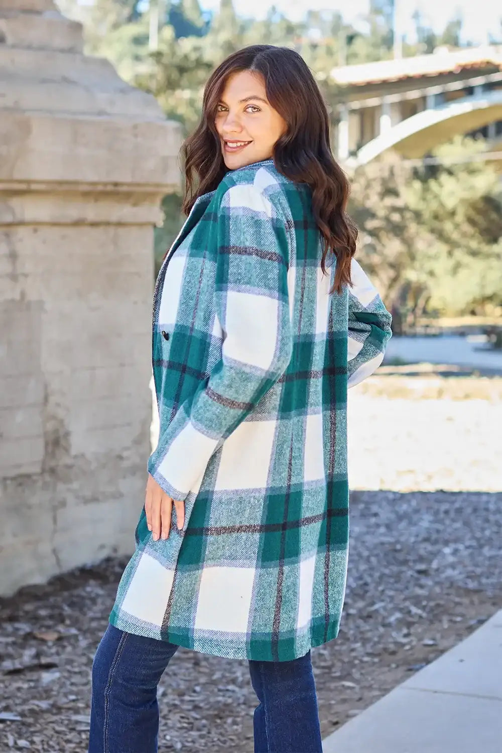 Woman wearing a plaid coat outdoors with trees and a building in the background