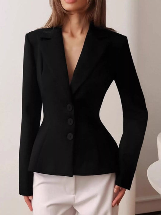 A woman wearing a fitted black blazer with structured shoulders, a deep V-neckline, and three front buttons, paired with white pants.