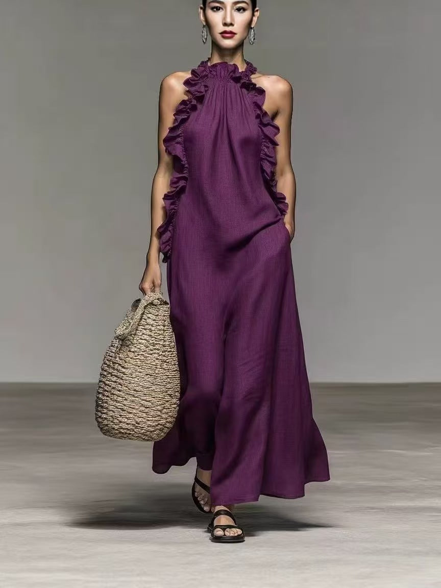 Woman wearing a purple ruffled jumpsuit holding a woven bag on a plain background