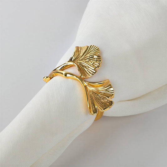 Gold metal ginkgo leaf napkin ring holding a white fabric napkin.