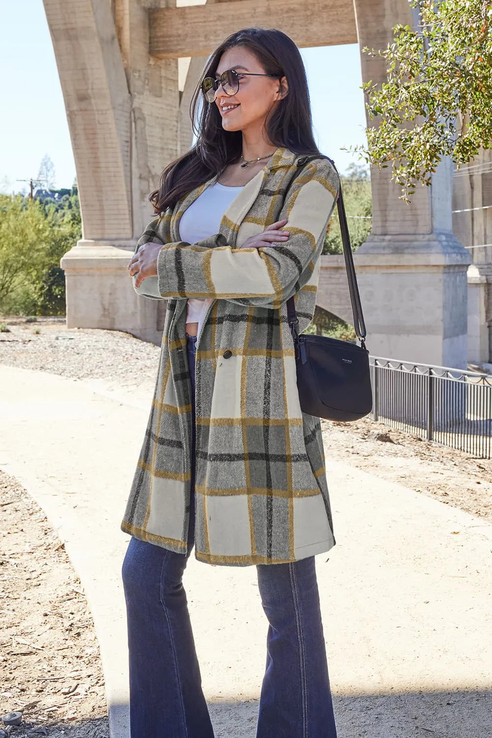 Woman wearing a plaid coat standing outdoors with a building and trees in the background.