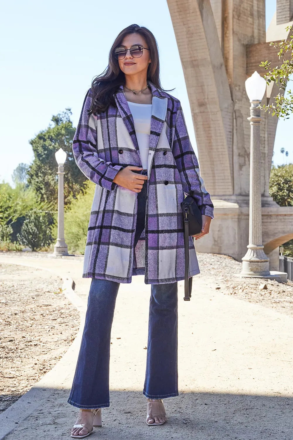 Woman wearing a purple plaid coat and blue pants standing outdoors.