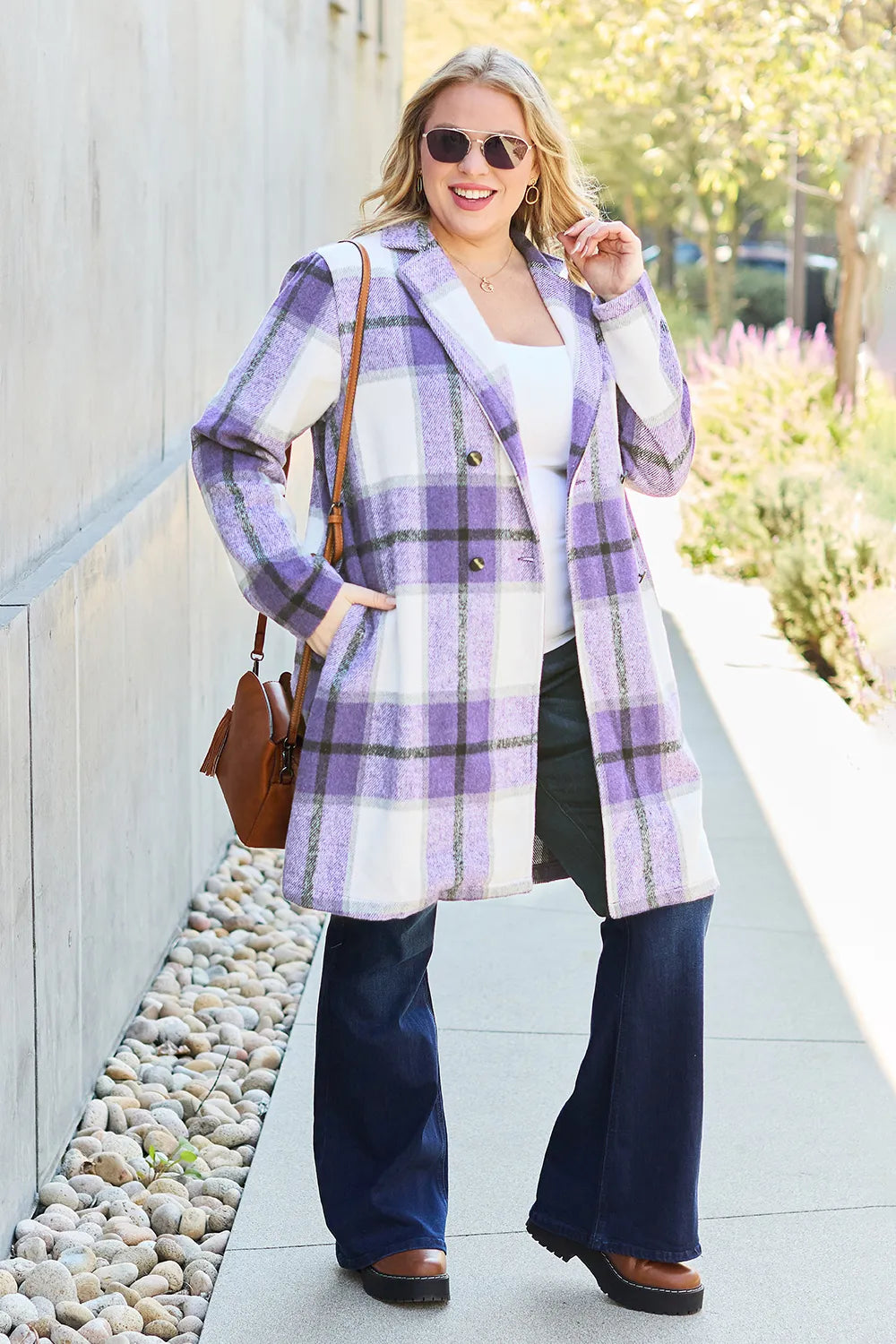 Woman wearing a purple plaid coat with a white shirt and blue pants, standing on a sidewalk.