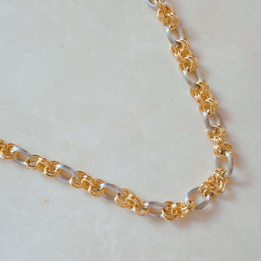 Two tone metal chain necklace with alternating gold and silver circular links on a light stone surface.