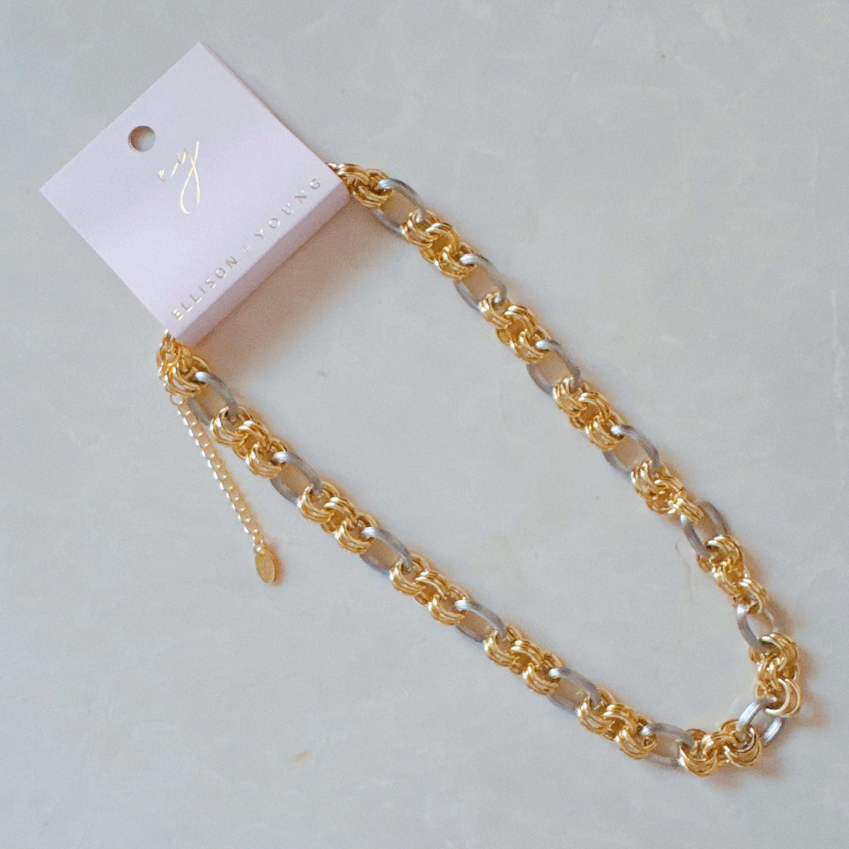 One two-tone metal chain necklace with interlocking gold and silver links on an ELLISON + YOUNG pink card.