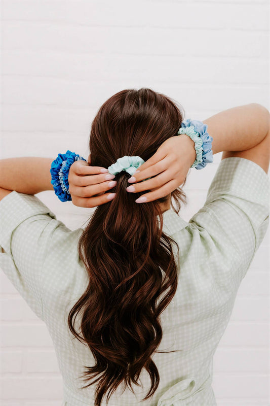 A woman wearing three Blue My Mind large silk scrunchies in shades of blue and mint on her hair and wrists.