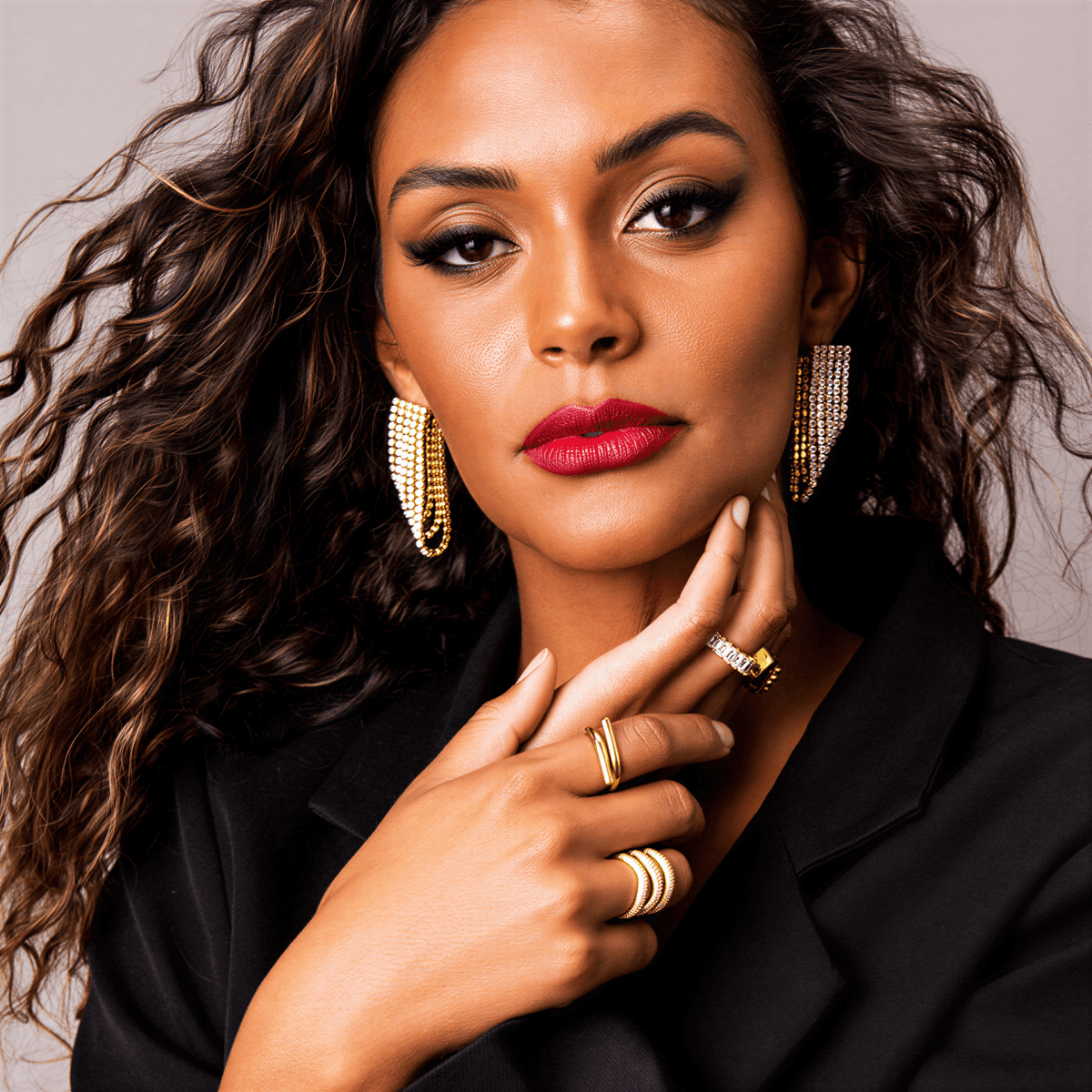 A woman wearing gold Elle Pave Rings and matching drop earrings, posing with her hands near her face.