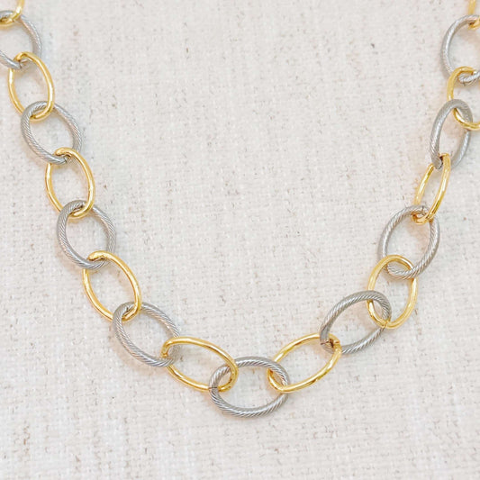 Two-tone metal necklace with alternating smooth gold and cabled silver oval links on a white fabric background.