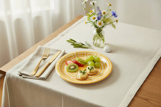 A round yellow paper plate with a classic Greek key geometric pattern printed in a lighter cream color, shown with food on a table.