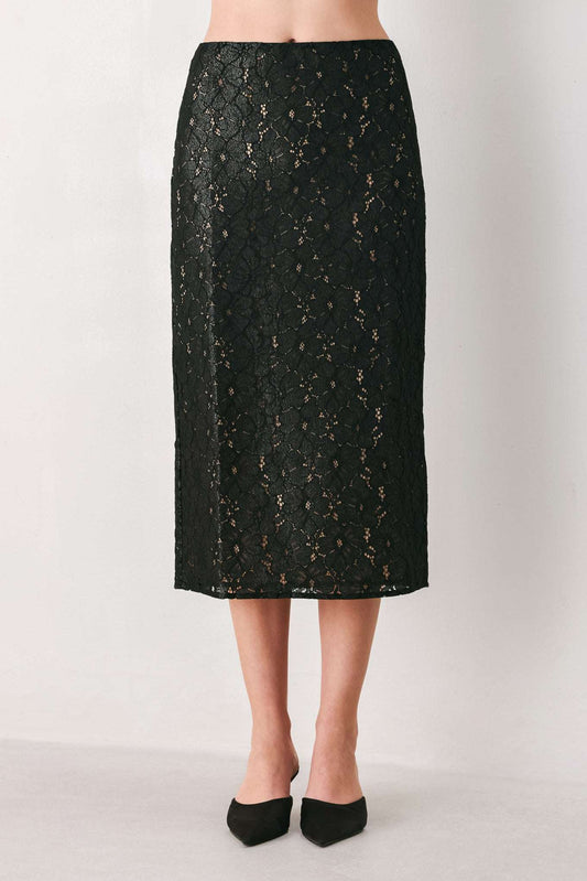 A black lace midi skirt with a subtle gold monogram pattern, shown on a model wearing black pointed-toe flats against a plain white studio background.