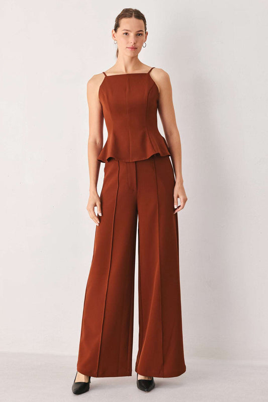 Woman wearing a rust brown fabric peplum tank top and matching wide-leg trousers with front seams.