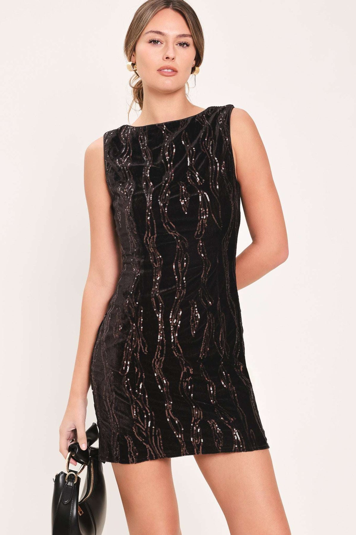 A woman modeling a sleeveless black sequined mini dress with a wavy metallic pattern, holding a small black handbag against a plain light background.