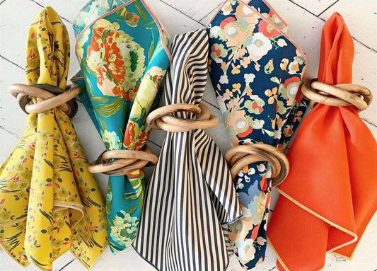 Five patterned and solid fabric napkins held by round wood rings, arranged in a row on a white surface.