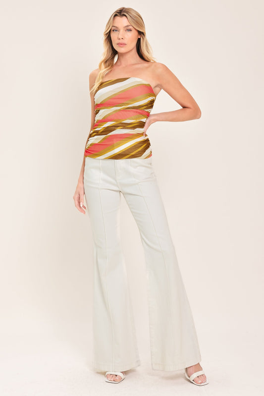 Woman wearing a strapless, multicolored top and white pants on a plain background