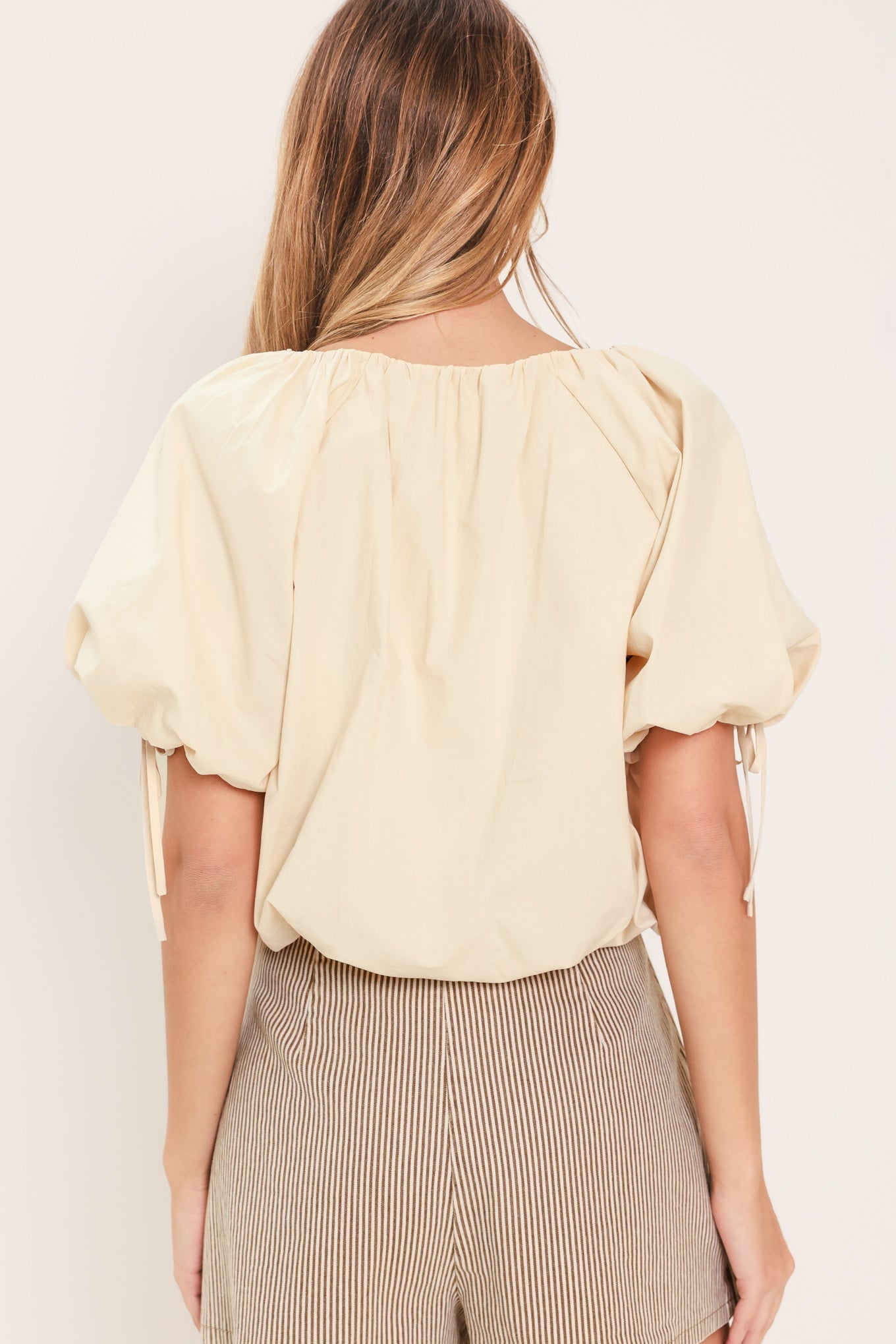 Woman wearing a light yellow blouse with puffed sleeves against a beige background
