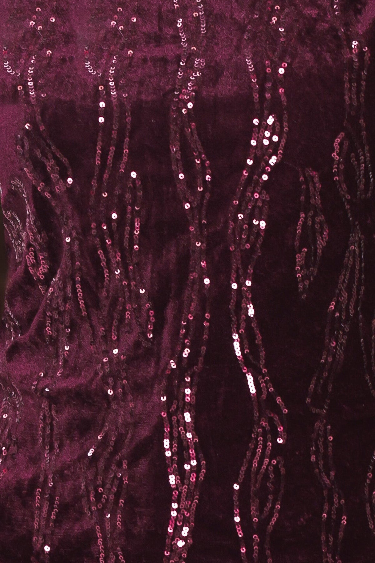 A close-up of deep magenta velvet fabric adorned with vertical strands of shimmering pink and silver sequins.