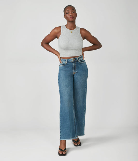 Woman wearing a gray tank top and blue jeans on a white background