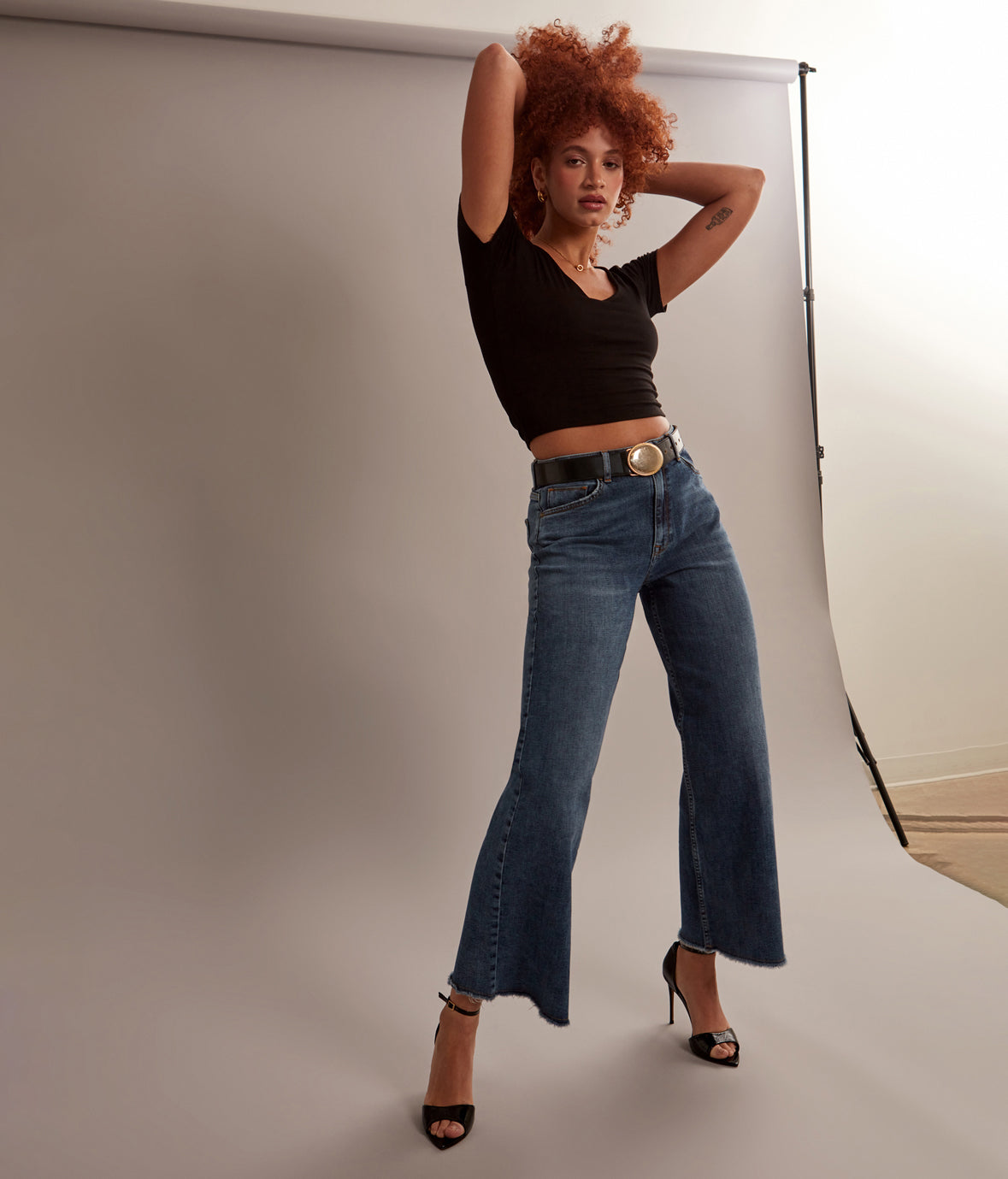Woman posing in a studio setting wearing a black top and blue jeans.