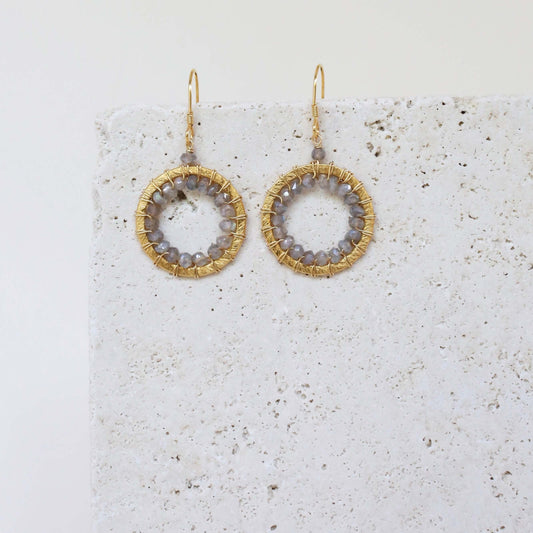 Gold hoop earrings with circular designs on a textured white surface