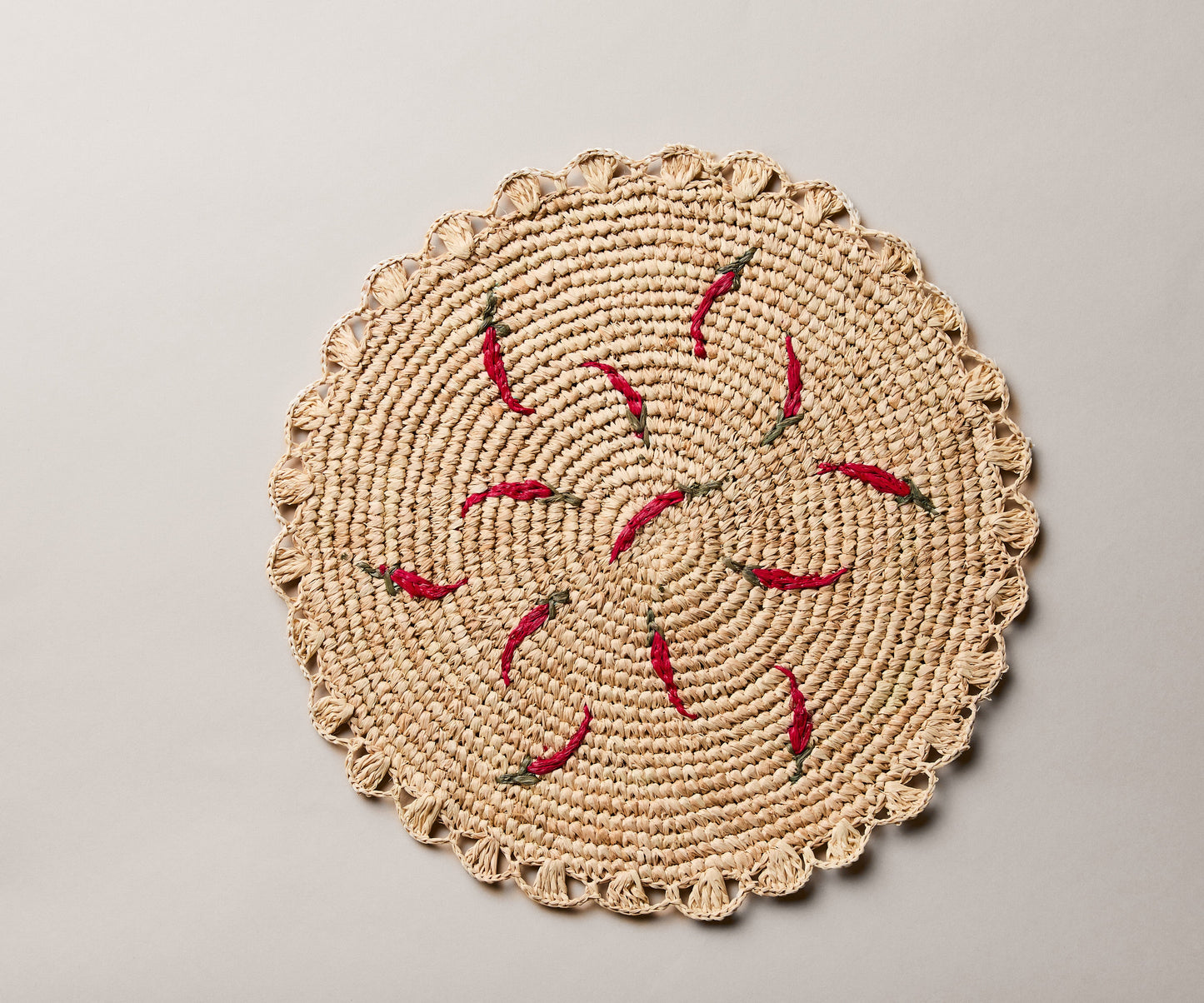 Scattered chili handwoven raffia round placemat with red chili pepper designs on a natural woven background.