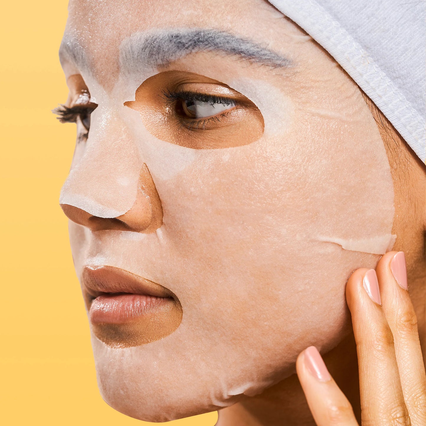 Person applying a face mask with a yellow background