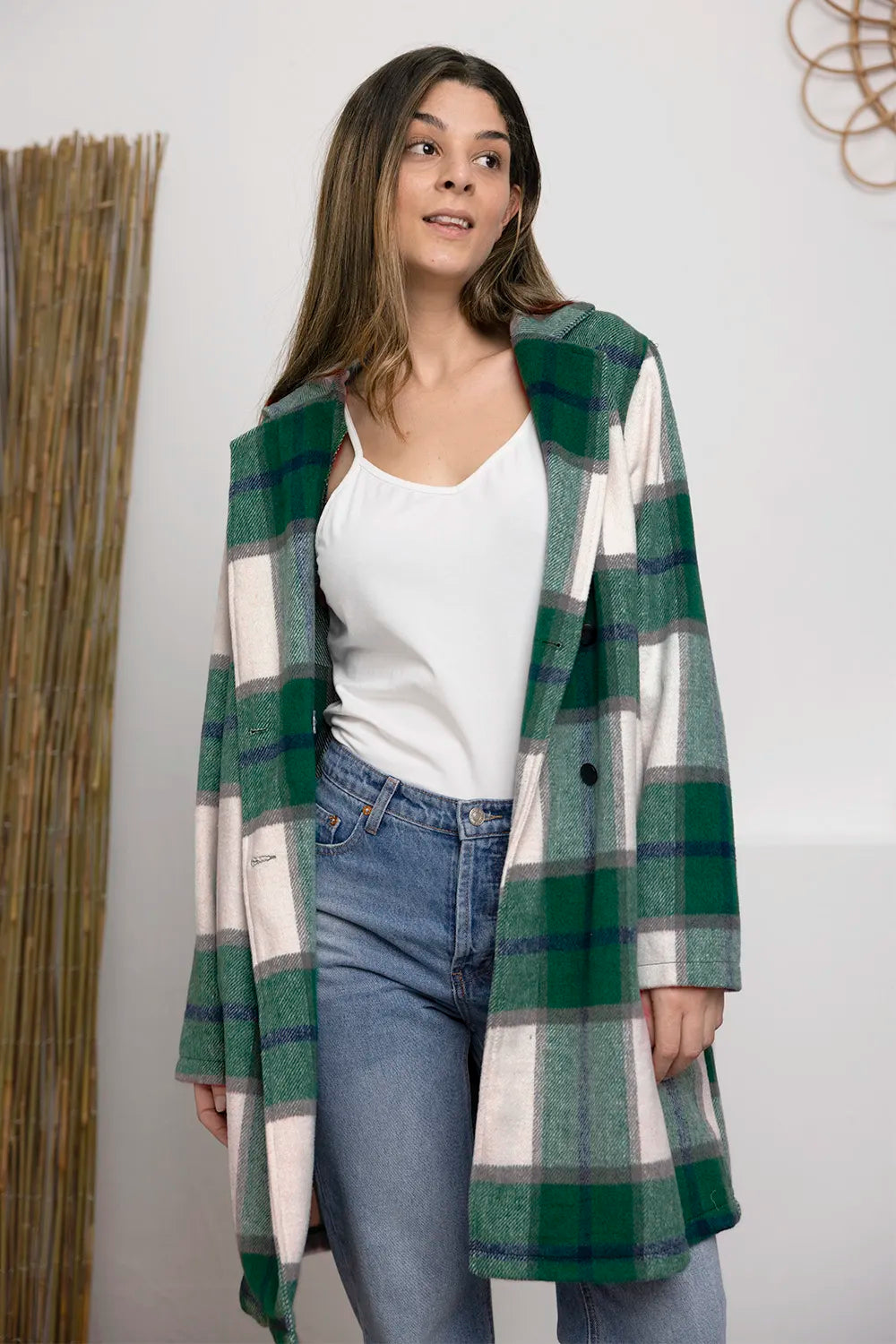 Woman wearing a green and white plaid coat over a white shirt and blue jeans against a plain background