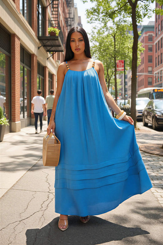 Woman wearing a blue dress holding a woven bag on a city street.