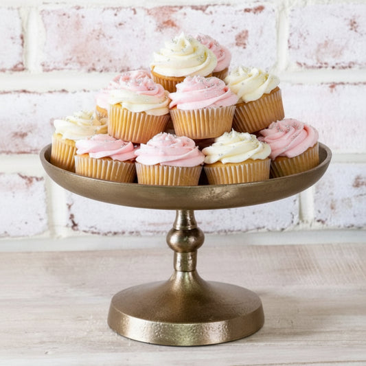 Bronze cake stand with cupcakes on a light wooden surface and white brick wall background