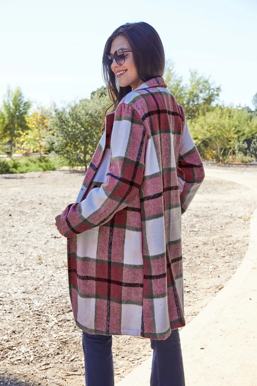 Woman wearing a plaid coat outdoors with trees in the background