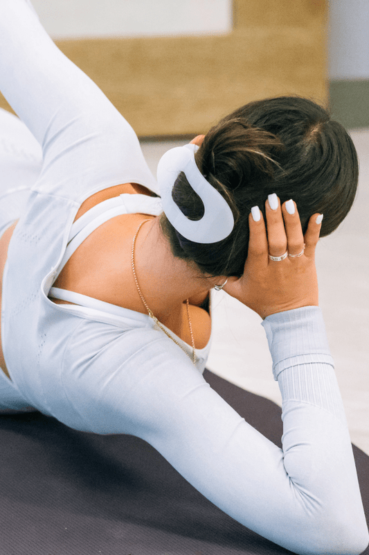One white flat round plastic hair clip holding a brunette bun, worn by a person in light blue athletic wear on a yoga mat.