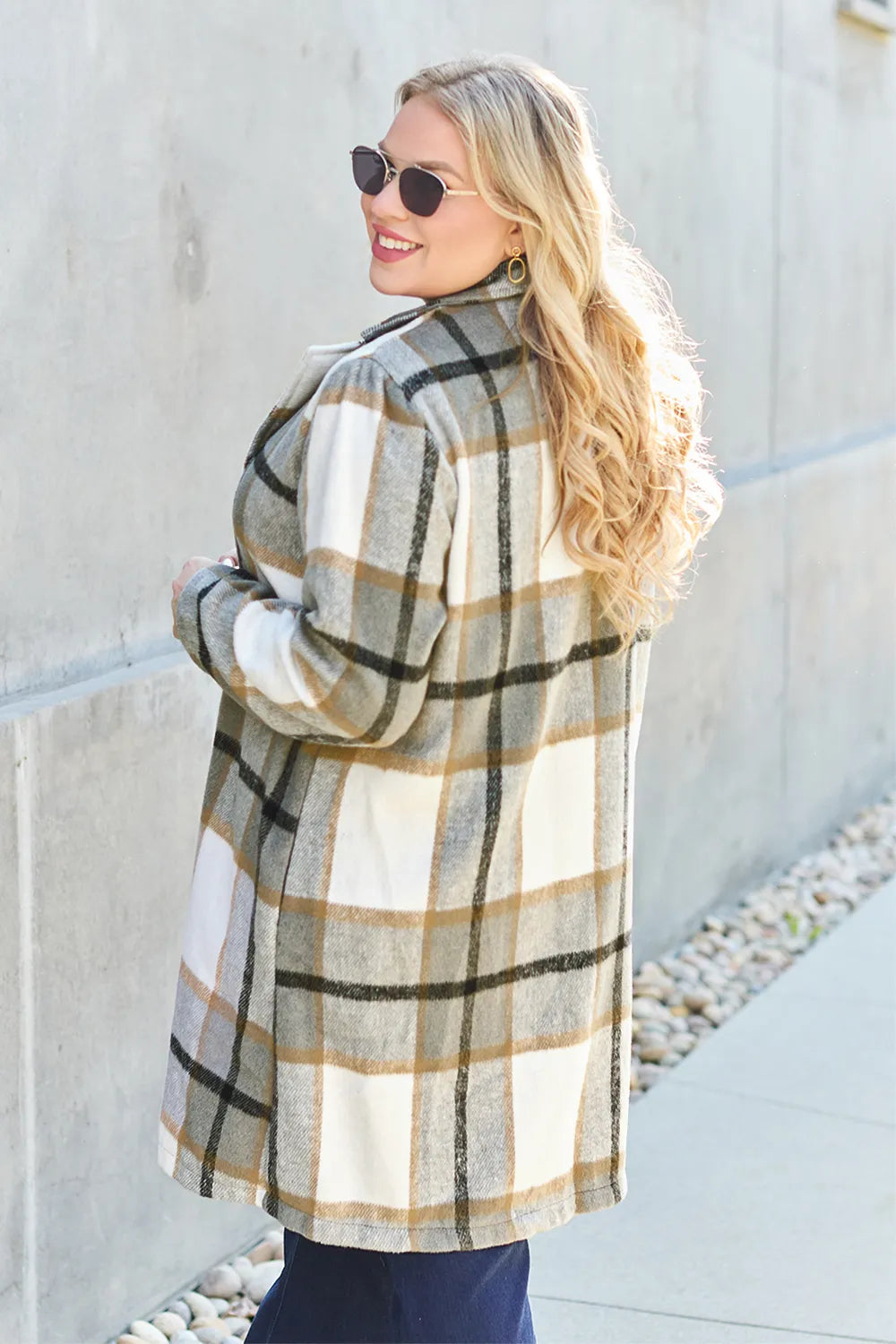 Woman wearing a plaid coat standing against a light-colored wall.