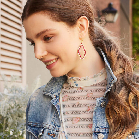 Woman wearing a denim jacket and floral top with red earrings, standing outdoors.