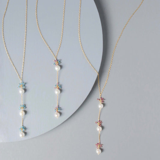 Two pearl necklaces with floral pendants on a gray background