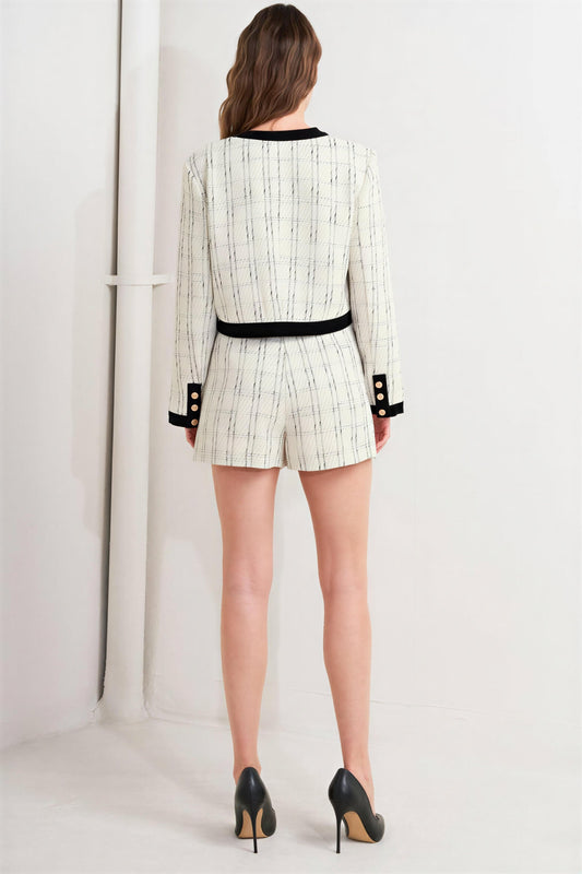 Rear view of a person wearing a white and black patterned fabric jacket and matching shorts with black heels.