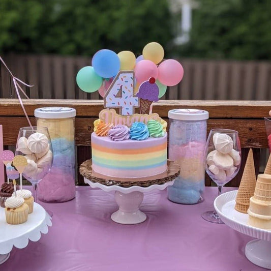 Colorful birthday cake with balloons and ice cream decorations on a table with candy and desserts.
