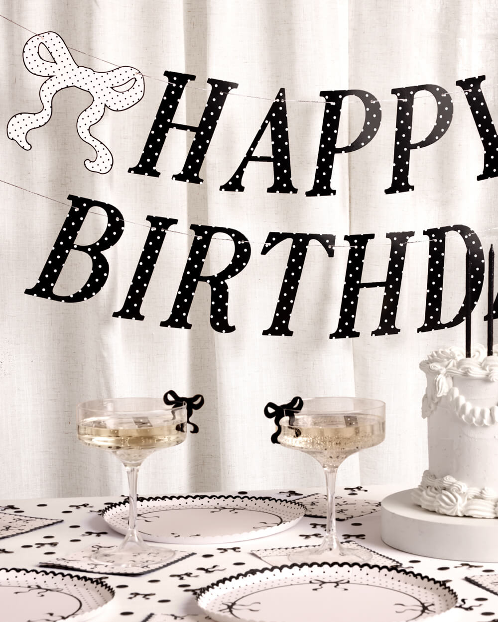 Decorative 'Happy Birthday' banner with a table setting featuring glasses and a cake.