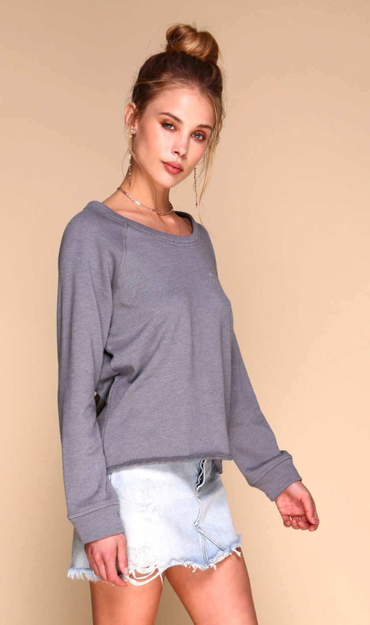 A woman modeling a gray long-sleeve crewneck sweatshirt with light-wash denim shorts against a solid beige studio background.