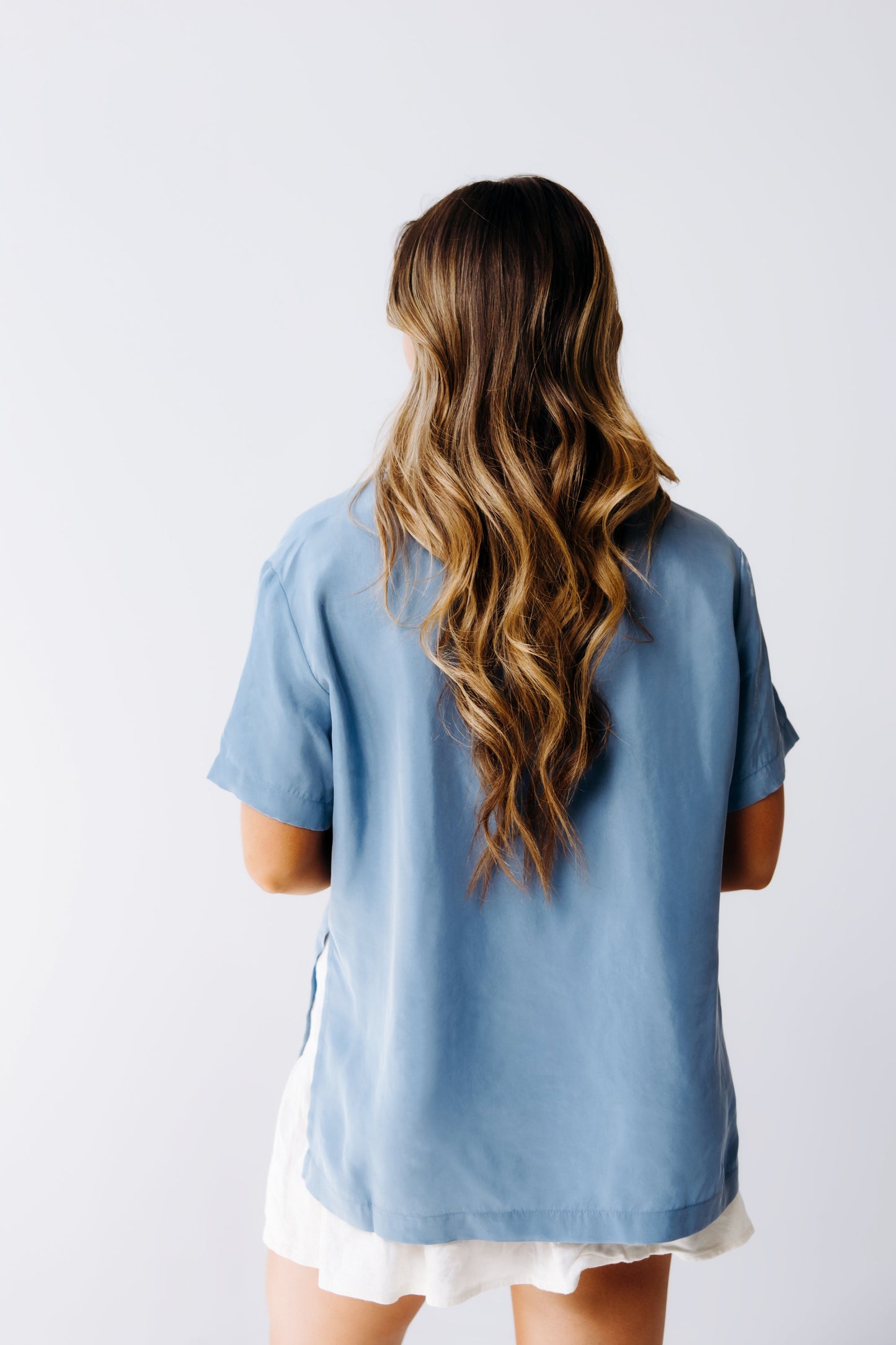 Person wearing a light blue shirt with long hair on a plain background