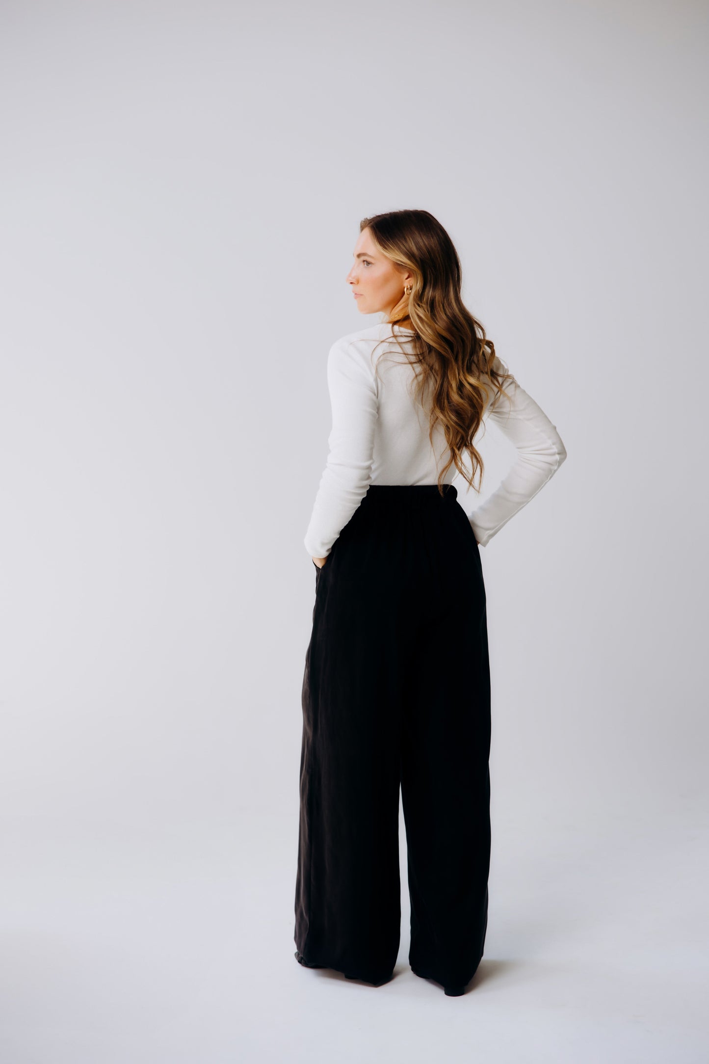 Woman wearing a white top and black wide-leg pants on a plain background
