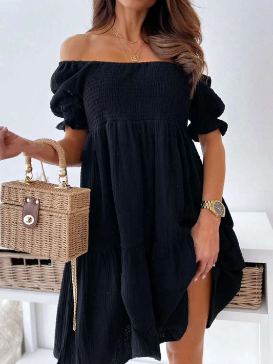 Woman wearing a stylish off-shoulder black dress with a woven handbag for chic summer outfit inspiration